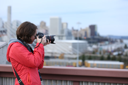 Side view of Woman in orange red coat holding camera to eye  in urban city setting