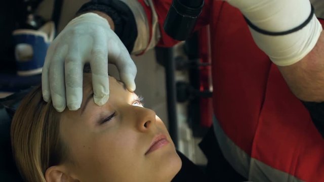 Experienced paramedic checking reaction of injured girl to light, concussion