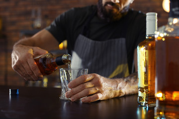 Bartender pouring whiskey into glass at counter in bar, closeup