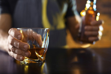 Bartender with glass and bottle of whiskey at counter in bar, closeup. Space for text