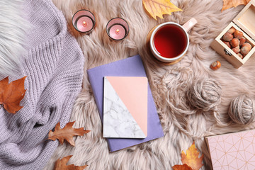 Flat lay composition with notebooks, cup of tea and warm clothes on fuzzy rug