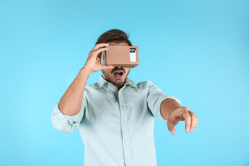 Fototapeta premium Young man using cardboard virtual reality headset on color background