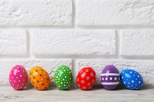 Decorated Easter eggs on table near brick wall. Space for text