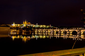 Fototapeta na wymiar Long exposure night photo, beautiful cityscape as seen from Charles Bridge, Prague towards the old center of of the Czech Republic capital, summer nighttime with water reflections from Vltava river