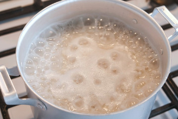 Rice is cooked in an aluminum sauce pan on a gas stove, close-up view.