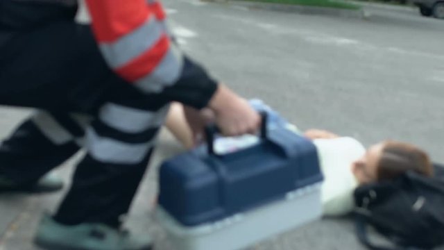 Doctor with first aid kit running to injured woman on street, crash victim, 911