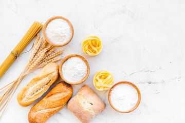 Farinaceous food. Fresh bread and raw pasta near flour in bowl and wheat ears on white stone background top view copy space