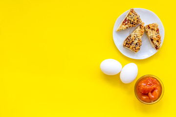 Ingredients for homemade cookies. Fresh cookies near jam, eggs on yellow background top view copy space