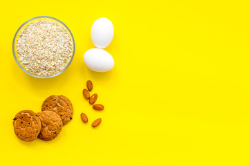 Ingredients for homemade oatmeal cookies. Fresh cookies near oatmeal and nuts on yellow background top view copy space