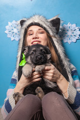 Obraz premium Pretty Woman In Fur Winter Hat Holding Little Cute shepherd puppy and smiling on blue background