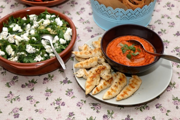 Chicken with roasted pepper sauce, feta cheese salad and tapenade bread rolls served on a table. Selective focus. 