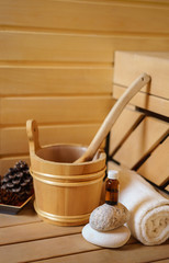 small private Finnish sauna setting with water bucket, oil essence, cones, hot stones and white towel on wooden background. wellness spa concept relax and treatment therapy. Close up, selective focus