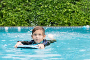 Fototapeta na wymiar Little boy learning to swim in swimming pool, practicing with foam pad.