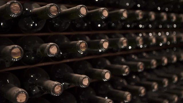 Rows of wine bottles without label on the shelf inside a cellar - closeup, tilt down blurry background