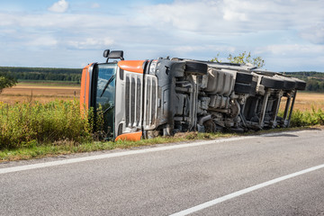 Overturned truck in field next to road, chassis visible