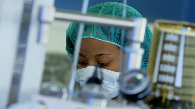 Professional Multi ethnic female Anesthesiologist monitoring anesthesia machine equipment during patient operation in hospital theater 