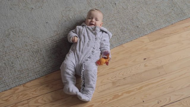 Medium shot of an adorable baby girl laying on the carpet of her living room at home, high point of view