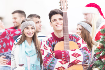 Young man with friends holding guitar on balcony on Christmas