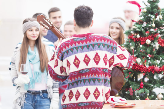 Young man with friends playing guitar on balcony on Christmas - Powered by Adobe