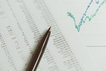 Fototapeta premium Investment, financial report statistic concept, close-up of black pen on printed stock exchange data price number or valuation table with green and blue yearly graph