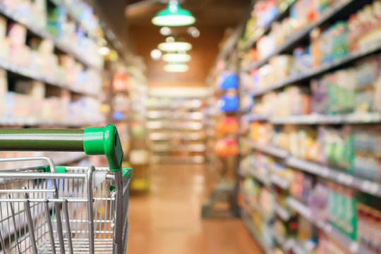 Empty green supermarket shopping cart with abstract blur grocery store aisle defocused background