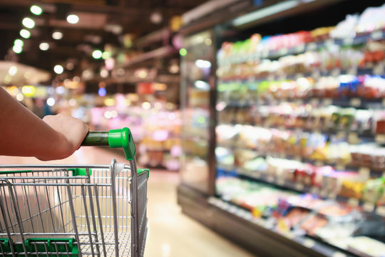 woman hand hold supermarket shopping cart with Abstract grocery store blurred defocused background with bokeh light