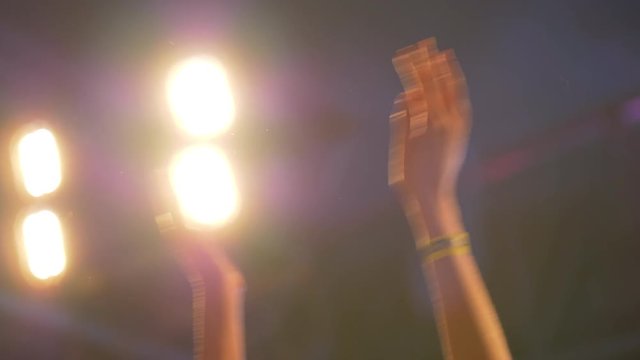 Close up slow motion shot of hands clapping with cheering fans at a live concert against bright lights