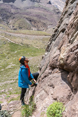 One man climber working with the rope belaying another climber while climbing a rock wall inside central Andes mountains at Santiago, Chile, we can see the rock climbing equipment, rope, helmet