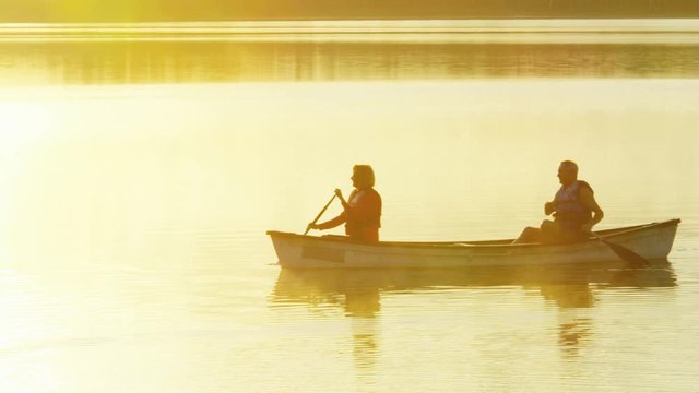 Silhouette of retired Caucasian American couple enjoying their outdoor lifestyle at sunset kayaking on the vacation resort lake 