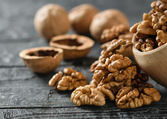 Peeled walnuts are poured from a wooden bowl onto a dark wooden table.