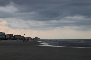 Beautiful beach waves surf horizon, turquoise blue reflecting water and storm clouds in gray sky.