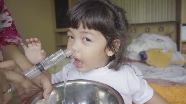 Video slow motion of Asian mother making nasal wash for her baby girl by flushing kid'nose with syringe and saline. An Irrigation can benefit people who have sinus problems,nasal allergies isolated on