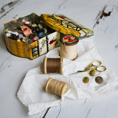 Cotton reels, button tin, buttons and scissors on lace edge handkercheif