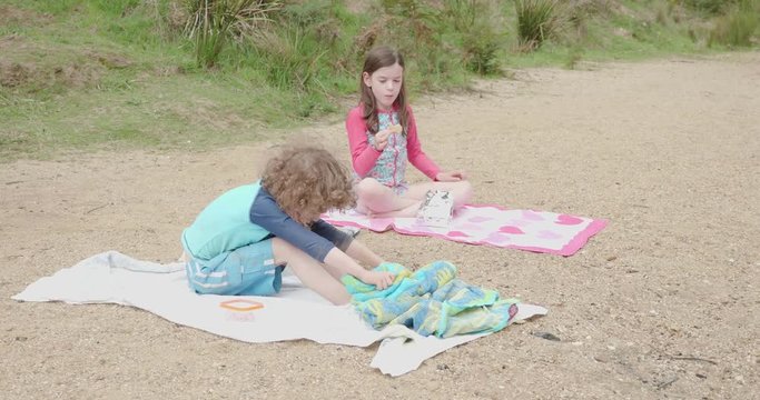 boy and girl sitting on beach towels, little girl eating a cookie and boy towelling his feet