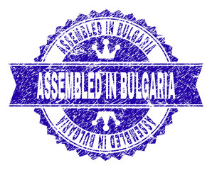 ASSEMBLED IN BULGARIA rosette seal imprint with distress style. Designed with round rosette, ribbon and small crowns. Blue vector rubber print of ASSEMBLED IN BULGARIA tag with dirty style.