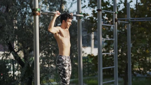 Athlete pulls up on the bar on the fitness area, side view.