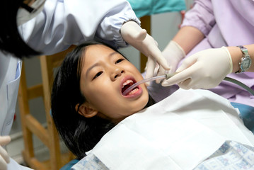 Obraz na płótnie Canvas Close up of young Asian Pre teen girl having dental professional treatment in stomatology clinic. Kid patient at dental office open mouth with suction. Dentist examining and cleaning her teeth.