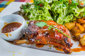 Honey Pork Ribs Served with Salad and Spicy Sauce in White Plate on Colorful Table