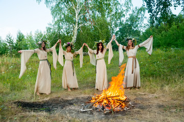 Attractive Women with Wreath of Flowers dancing around bonfire. Ivan Kupala Holiday Celebration. Russia