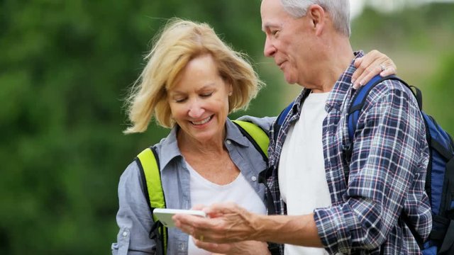 Happy retired Caucasian American couple watching picture on mobile enjoying their vacation hiking outdoors 