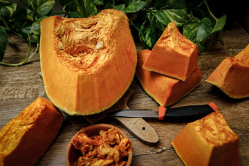 Pumpkin slices and seeds in the ceramic bowl on wooden table. Old kitchen board and orange/black...