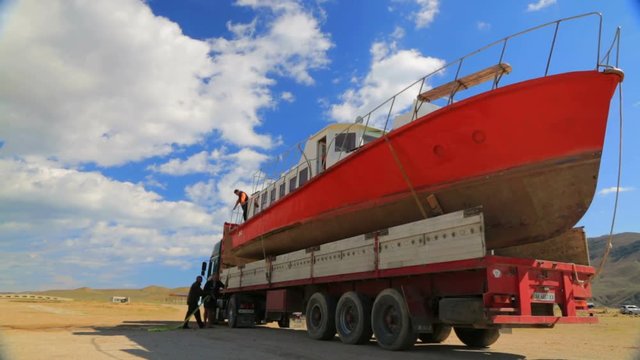 red boat on the truck, workers secure ropes
