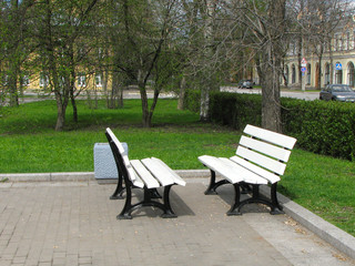 Fototapeta na wymiar Two white benches stand opposite each other in the park. Benches for friends.