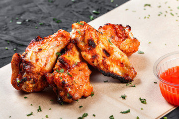 Fried chicken wings with bbq sauce on craft paper on black background. Hot Meat Dishes. Top view