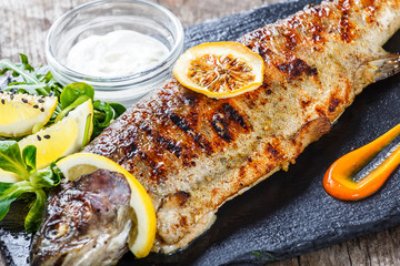 Grilled sea fish with lemon on stone slate background close up. Healthy food. Top view
