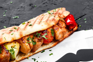 Sandwich from fresh pita bread with fillet grilled chicken and vegetables on dark wooden background. Shashlik or Shish kebab. Healthy lunch