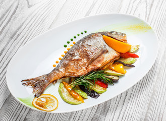 Grilled dorado fish with baked vegetables and rosemary on plate on wooden background close up. Healthy food. Top view