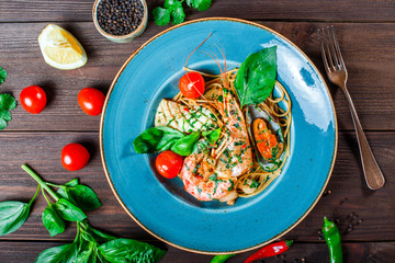 Italian pasta spaghetti with seafood, langoustine, mussels, squid, scallops, shrimp, Parmesan cheese, fresh basil and tomatoes on rustic wooden background. Mediterranean food. Top view