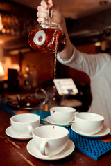 A transparent cup of black tea, a teapot and mint on a mirror table at a dark background