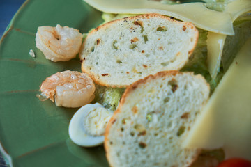 Fresh caesar salad with shrimps in a green plate on a light wooden table